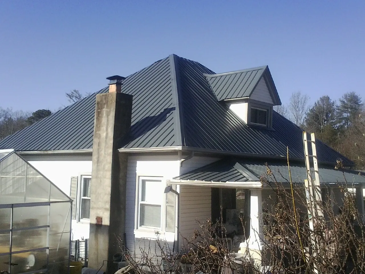Dark blue standing seam metal roof on a white farmhouse with dormer — Slate & Tile Roof Repair by Roofing Brothers in West River