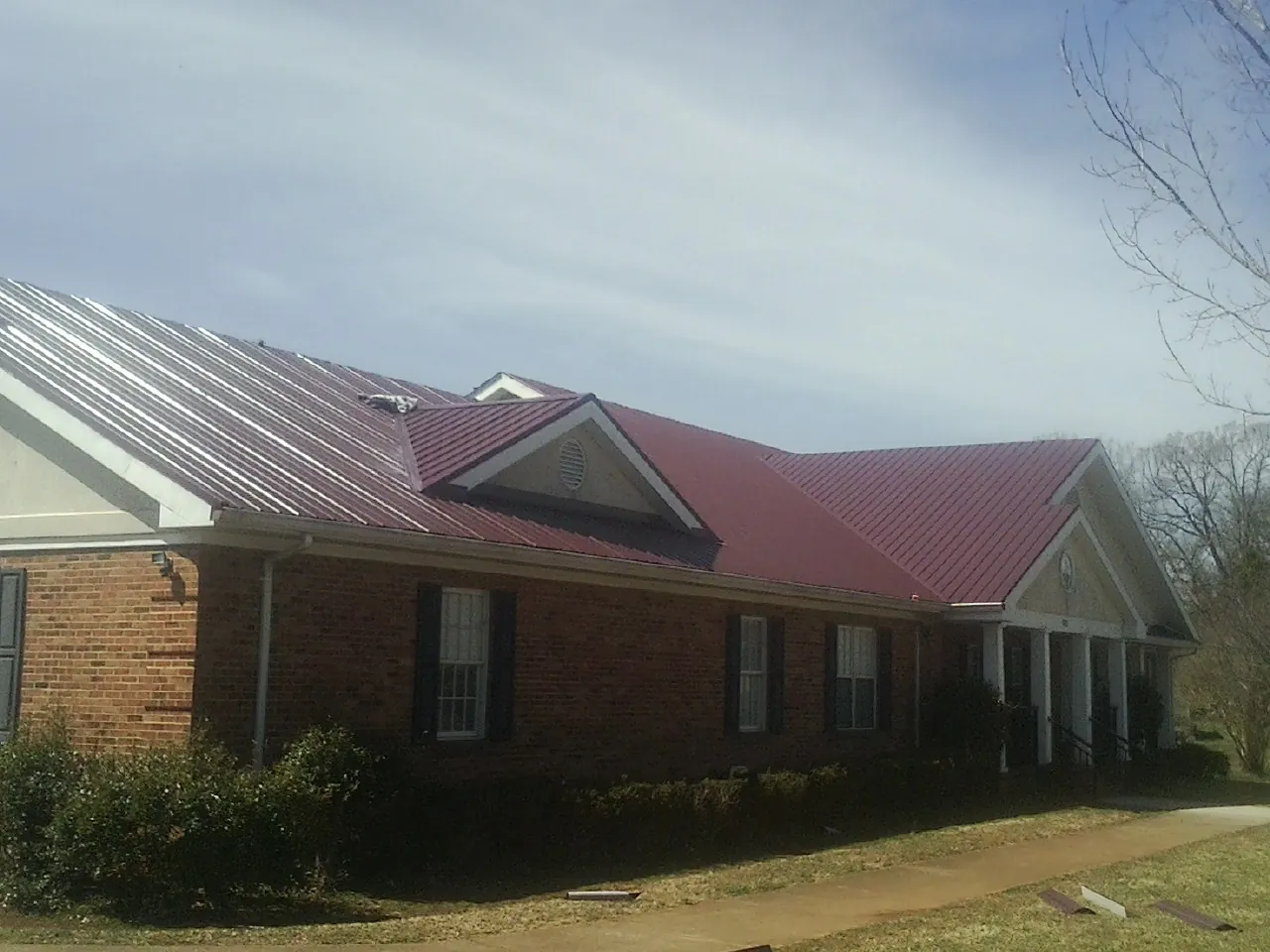 Red metal roof with gabled entries on a long brick building, from a Hail Damage Roof Repair job in West River