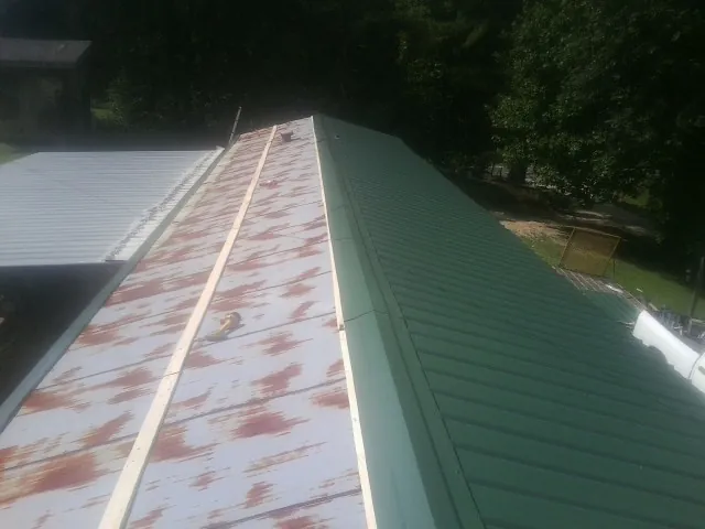 Old rusted panels beside newly installed green metal roofing — Wind Damage Roof Repair by Roofing Brothers in West River