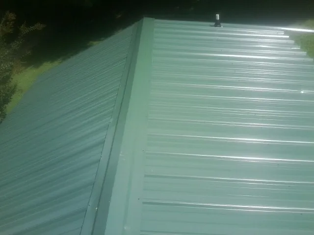 New green metal panels meeting at the ridge of a roof — Flat Roof Repair work by our crew in West River