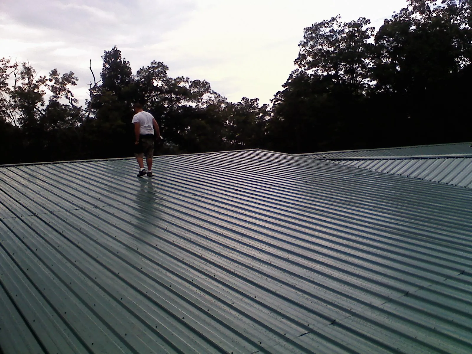 Roofer walking a wide expanse of new green metal roofing in West River