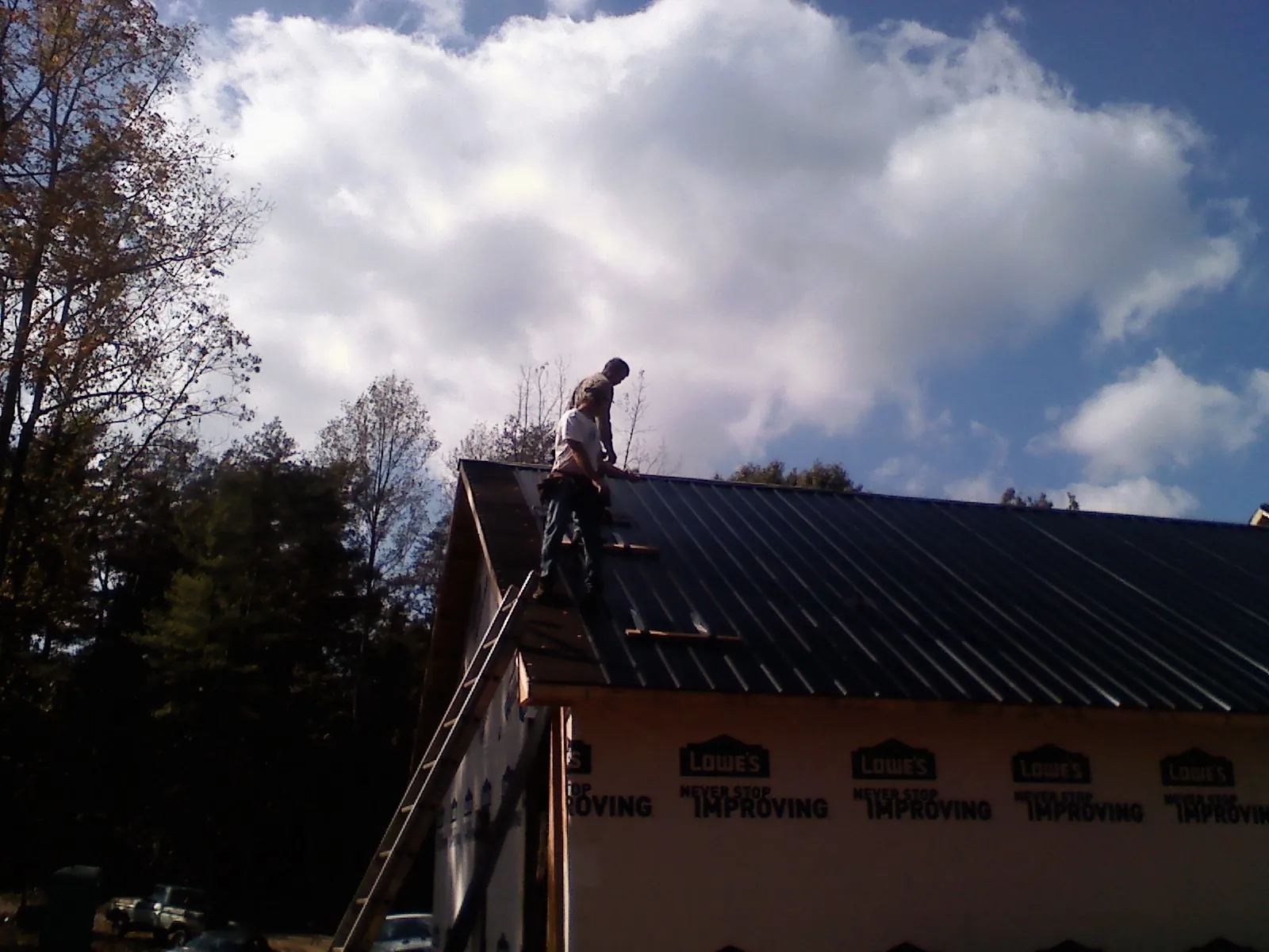 Roofer fastening dark metal panels high against a cloudy sky, from a Roof Inspection job in West River