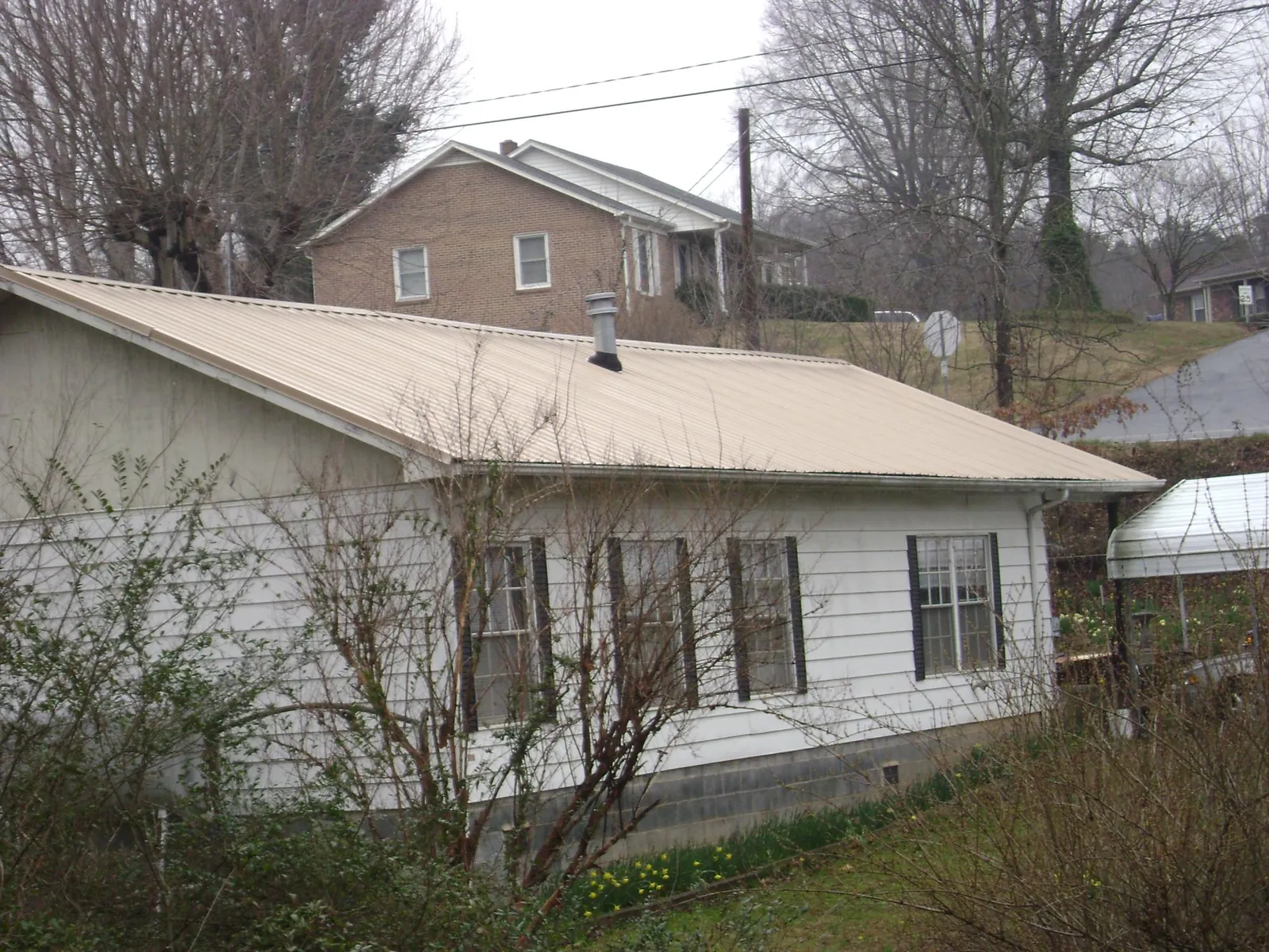 Tan metal roof on a white sided house set into a hillside — Commercial Roofing by Roofing Brothers in West River