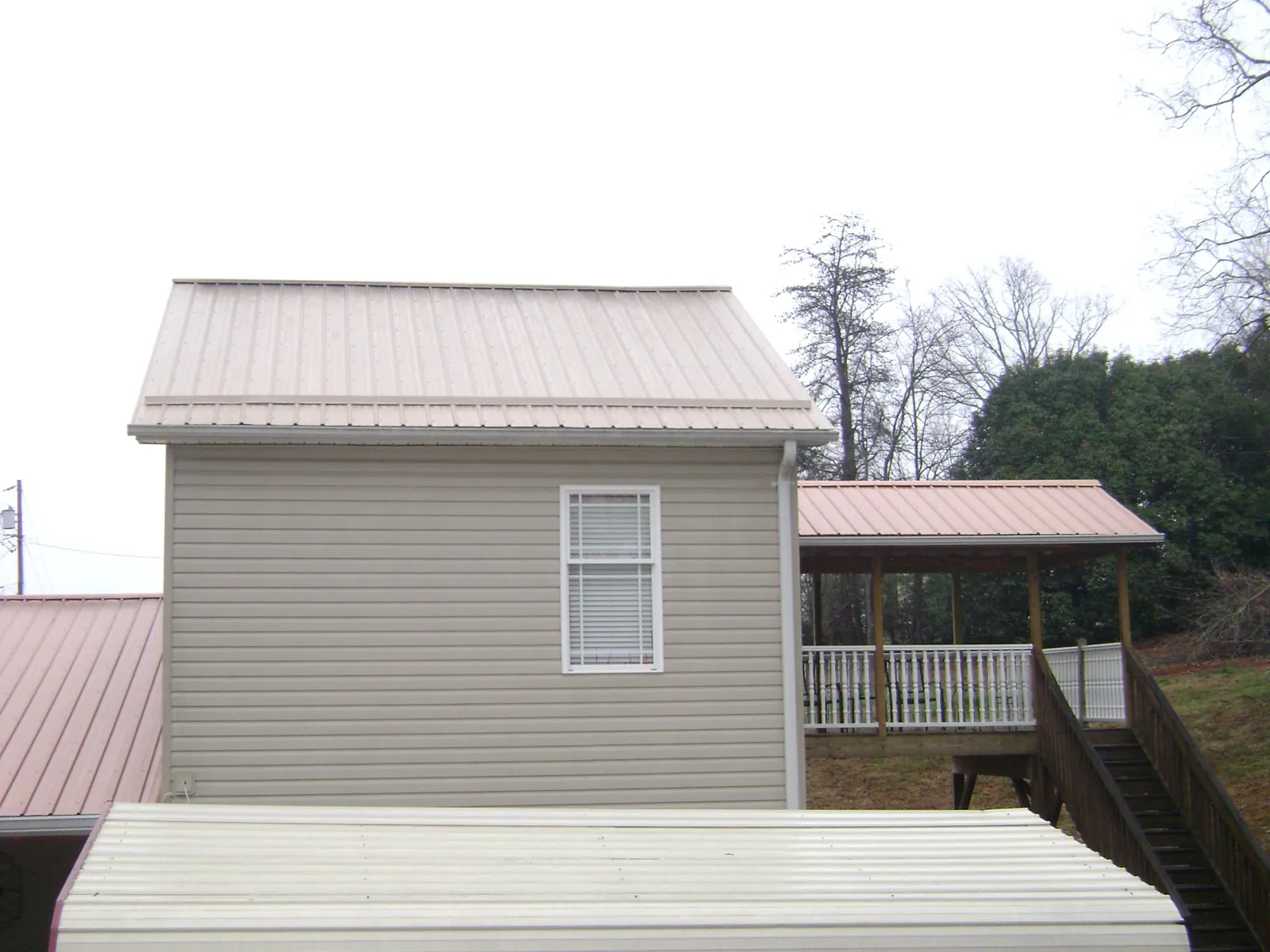 Tan metal roofs on a two story addition and attached porch, from a Roof Replacement job in West River
